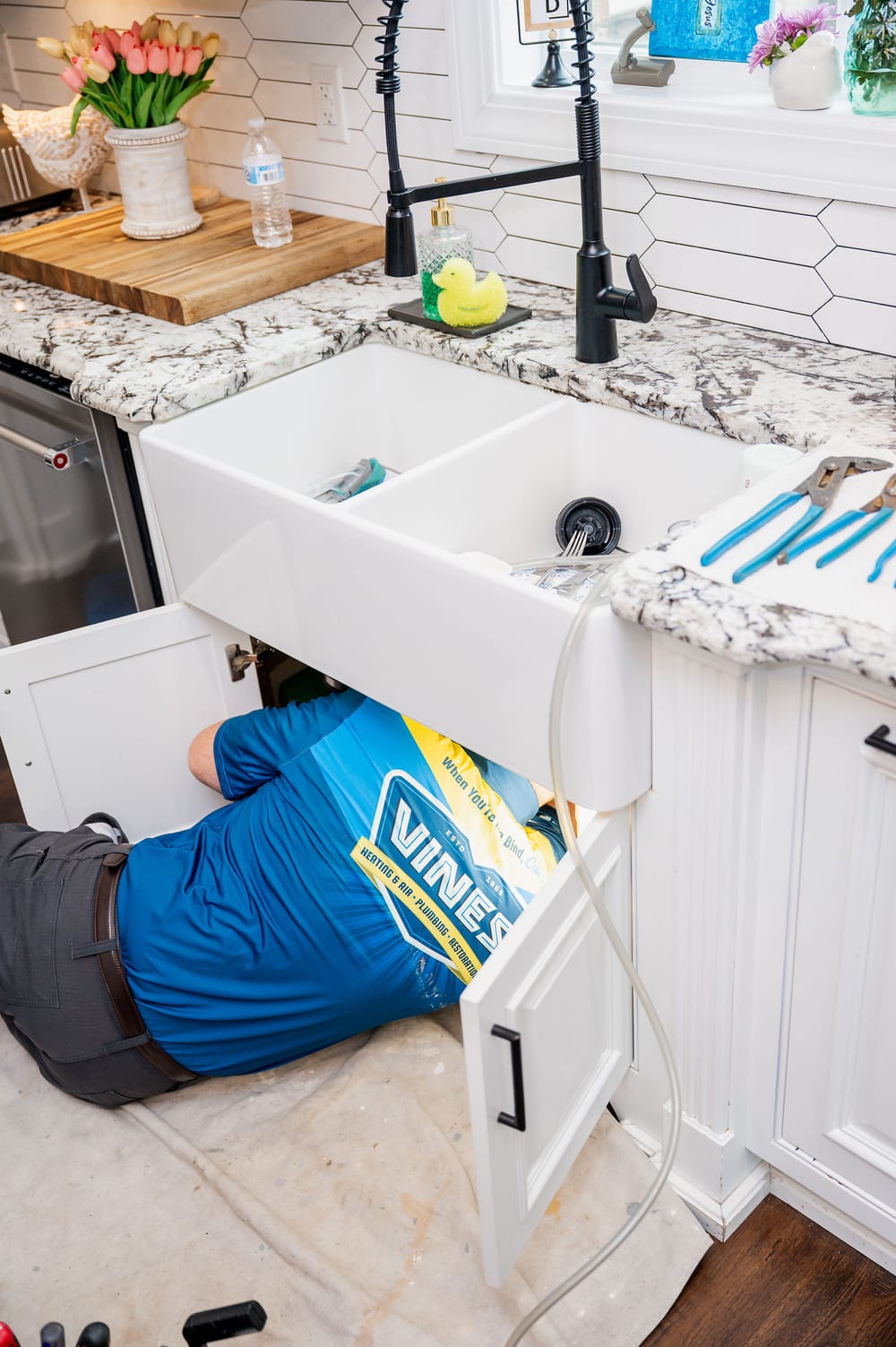 Vines plumber underneath sink to conduct drain cleaning.