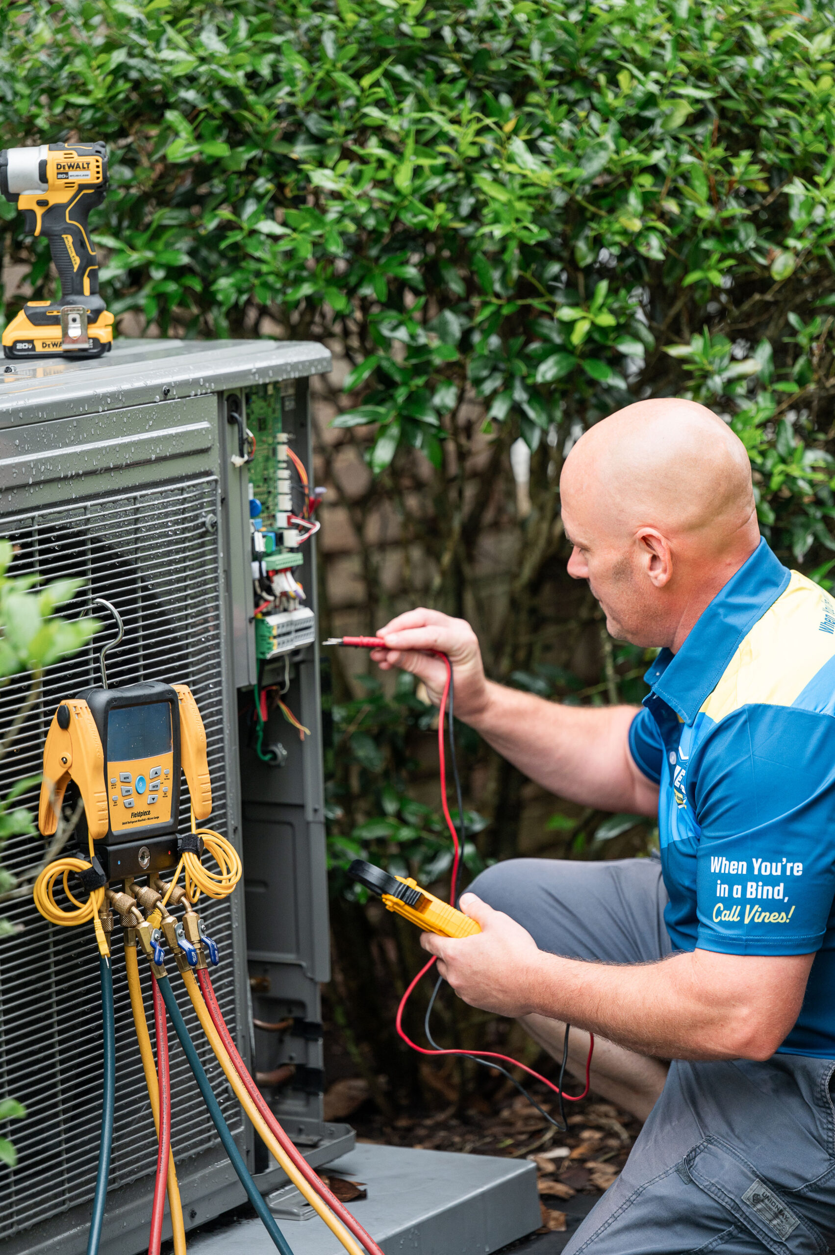 HVAC technician in blue shirt performing AC maintenance on outdoor unit