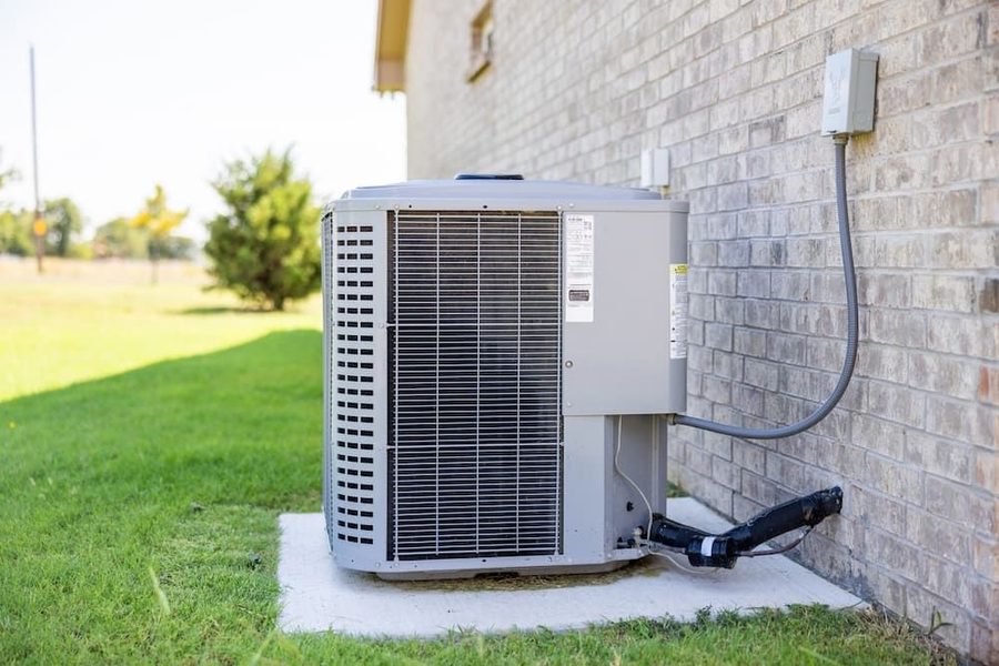 Outdoor air conditioner on a concrete slab with grass and trees in the background.