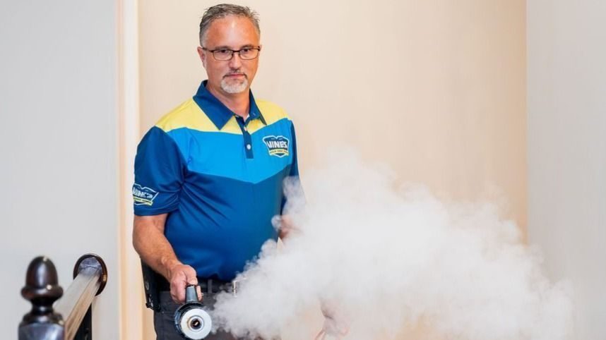 Employee in a blue and yellow work shirt standing in a home after a fire; restoration service concept. He is using fire restoration equipment.