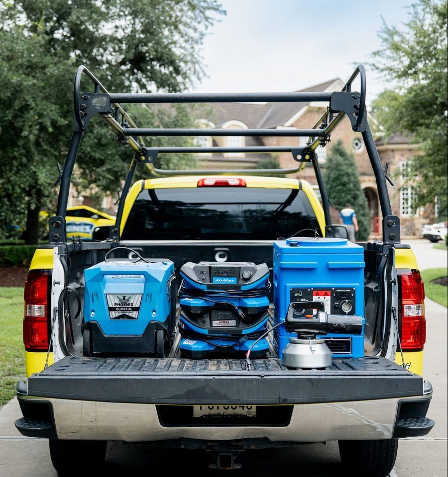 Yellow pickup bed loaded with power tools: two blue generators and a blue air compressor, plus a blue toolbox on a residential street.